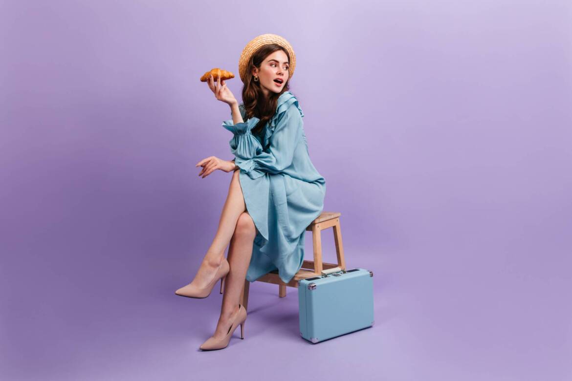 full-length-shot-young-lady-elegant-blue-dress-woman-sits-stool-suitcase-holds-delicious-croissant.jpg